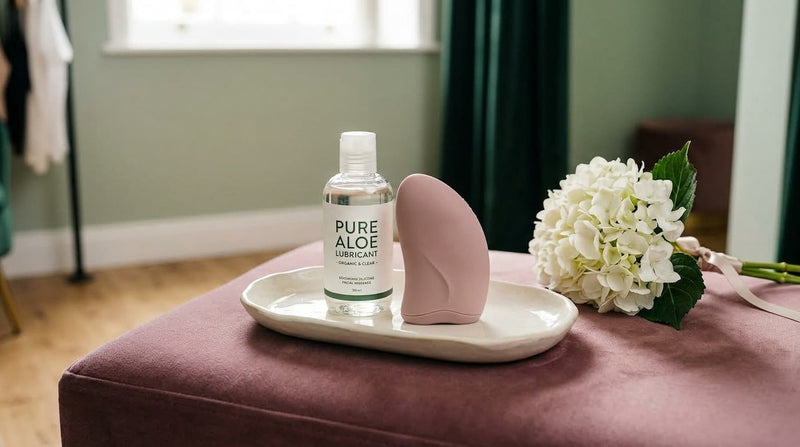 Curated intimate wellness collection at Belle Lacet boutique featuring body-safe aloe lubricant and a discreet massage device on a mauve velvet ottoman.
