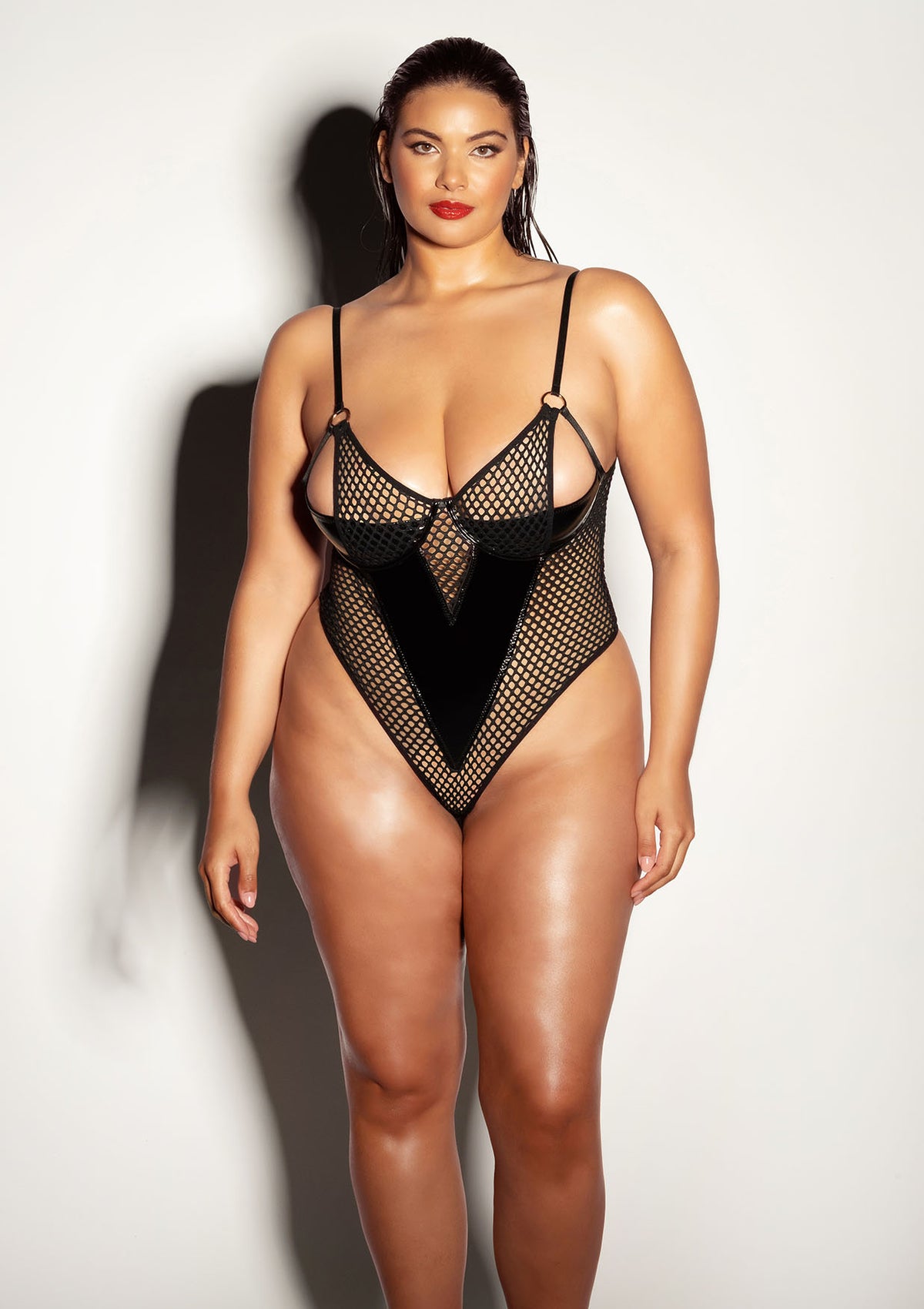 Woman wearing a vinyl and fishnet peek-a-boo teddy with underwire shelf cups and thong back