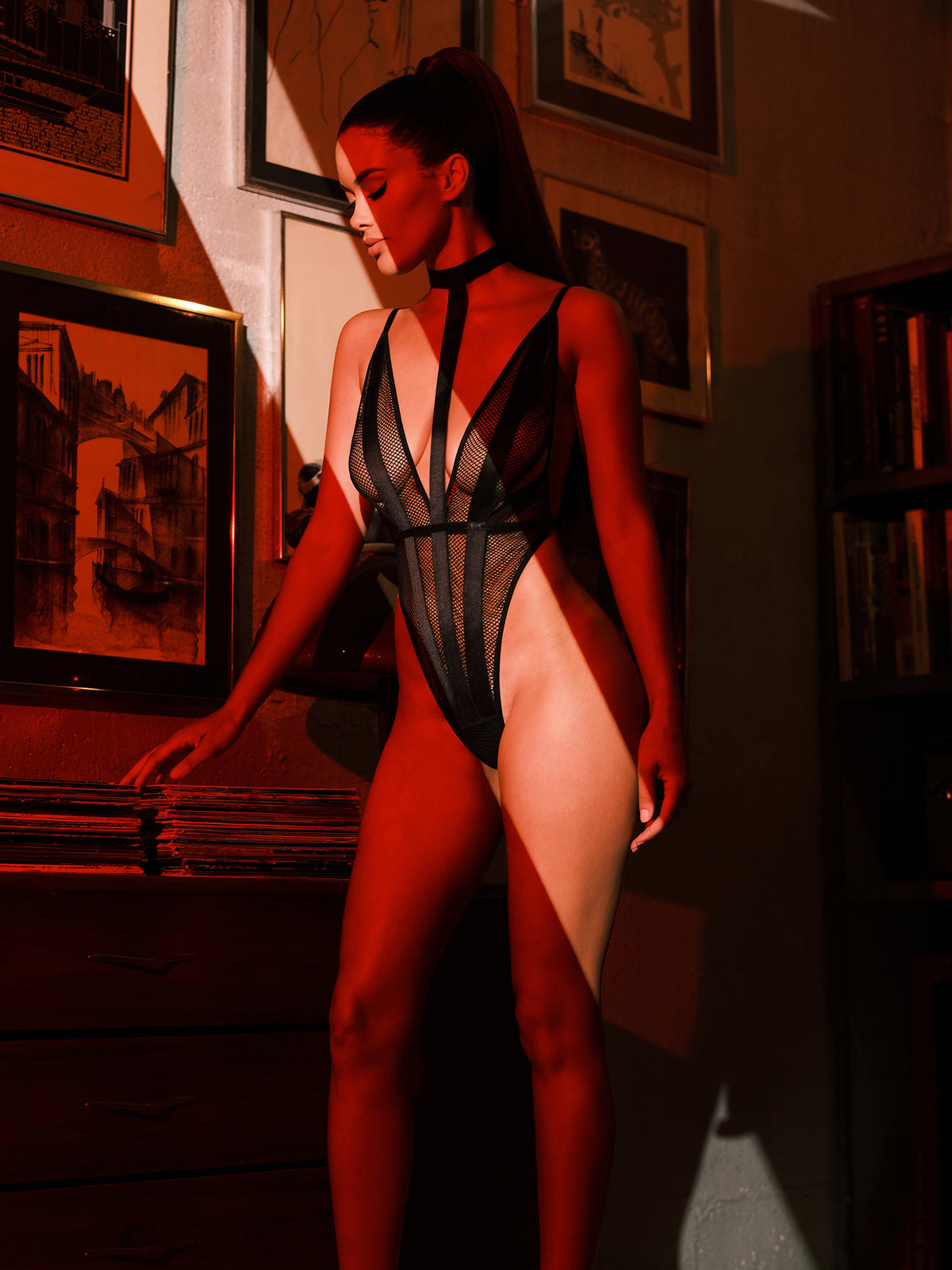 Person wearing a black mesh lingerie set in a room with framed pictures on the wall.