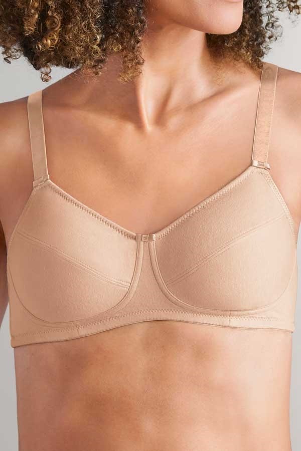 Woman wearing a beige wire-free soft cup bra with cotton pockets and adjustable straps for gentle support.
