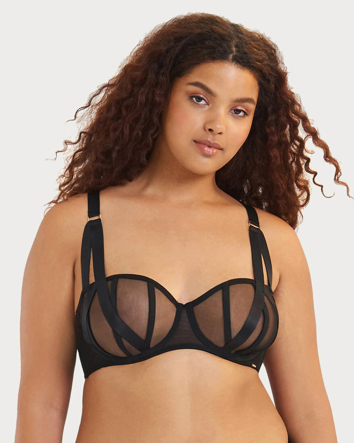 Woman wearing a black bralette with mesh panels on a plain background