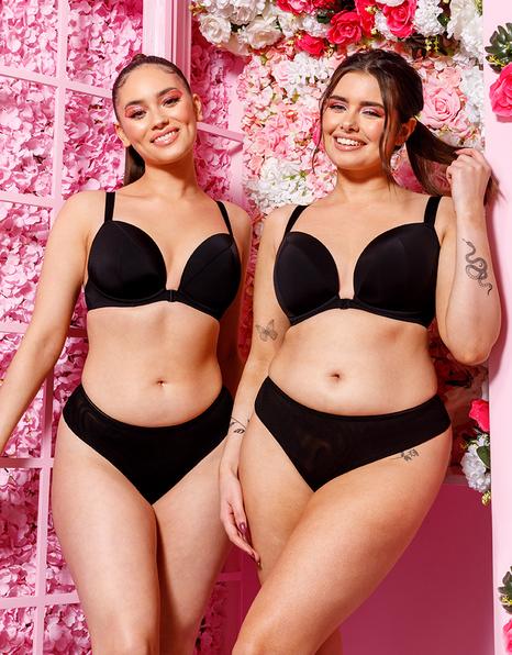 Two women wearing black lingerie against a pink floral background