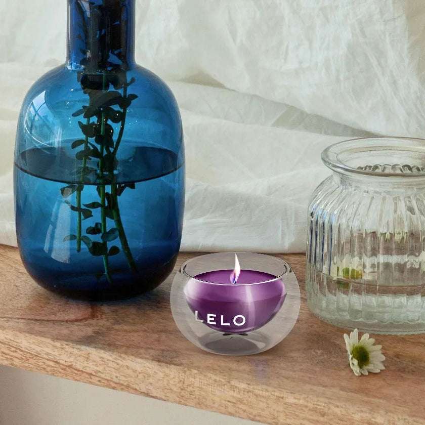 Blue vase, small glass container, and purple candle on a wooden surface with white fabric in the background
