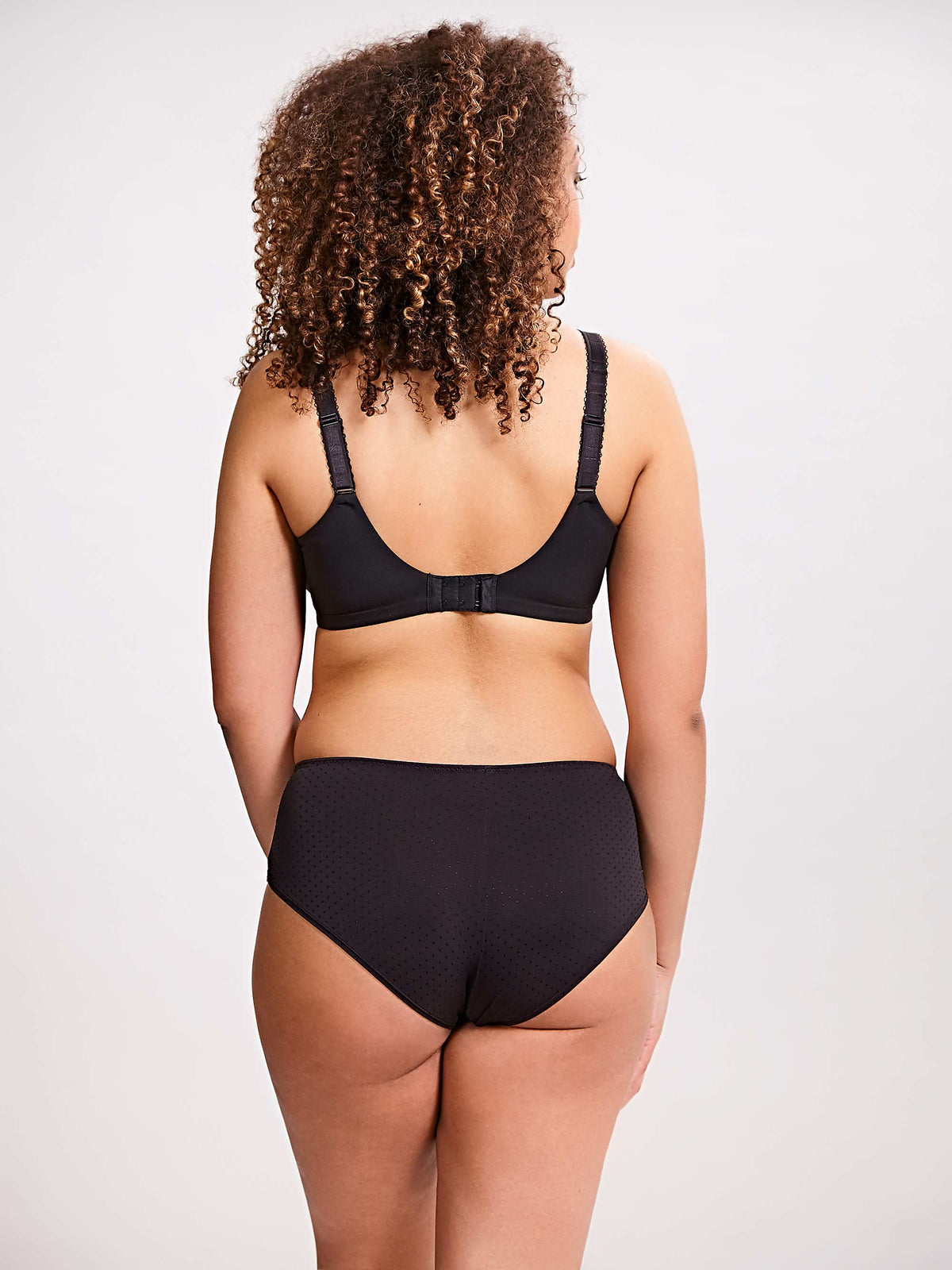 Person wearing a black bra and high-waisted underwear set on a plain background