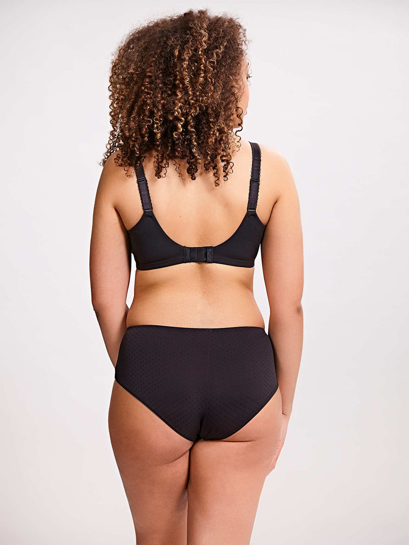 Person wearing a black bra and high-waisted underwear set on a plain background