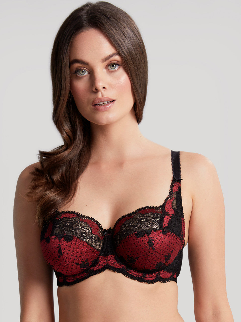 Woman wearing a red and black lace bra against a plain background