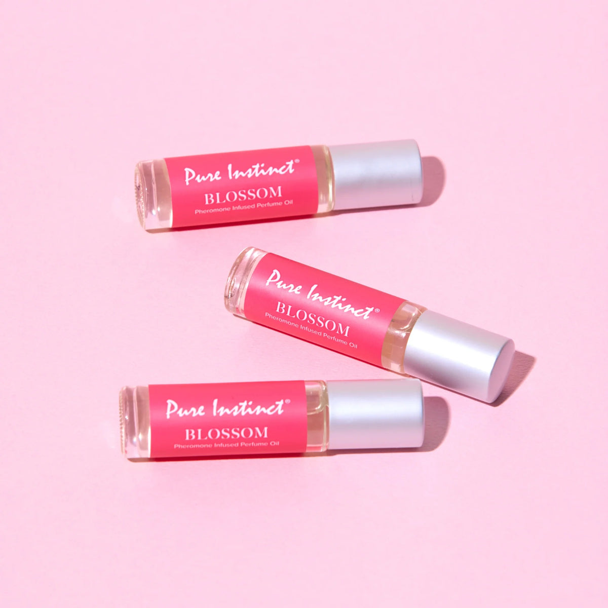 Three bottles of 'Pure Instinct Blossom' perfume on a pink background