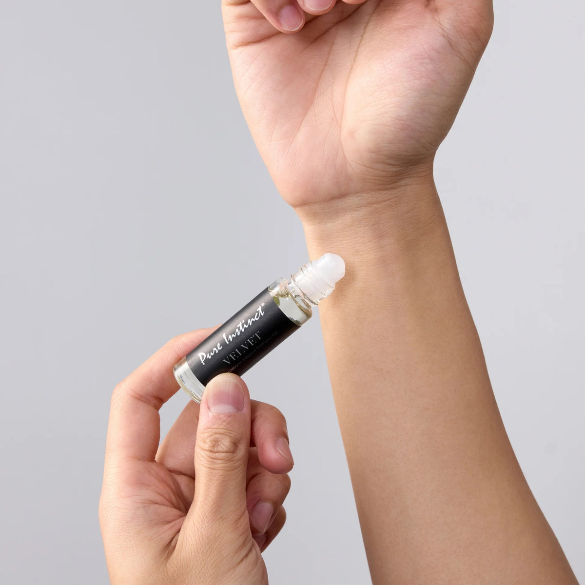 Hand holding a small rollerball bottle labeled 'Pure Instinct' against a gray background