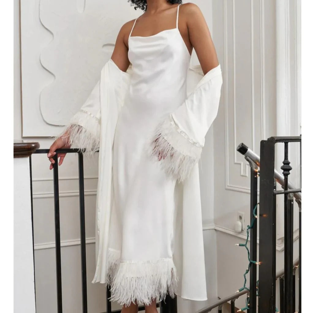 Woman wearing a white dress with feathered sleeves and hem in an indoor setting.