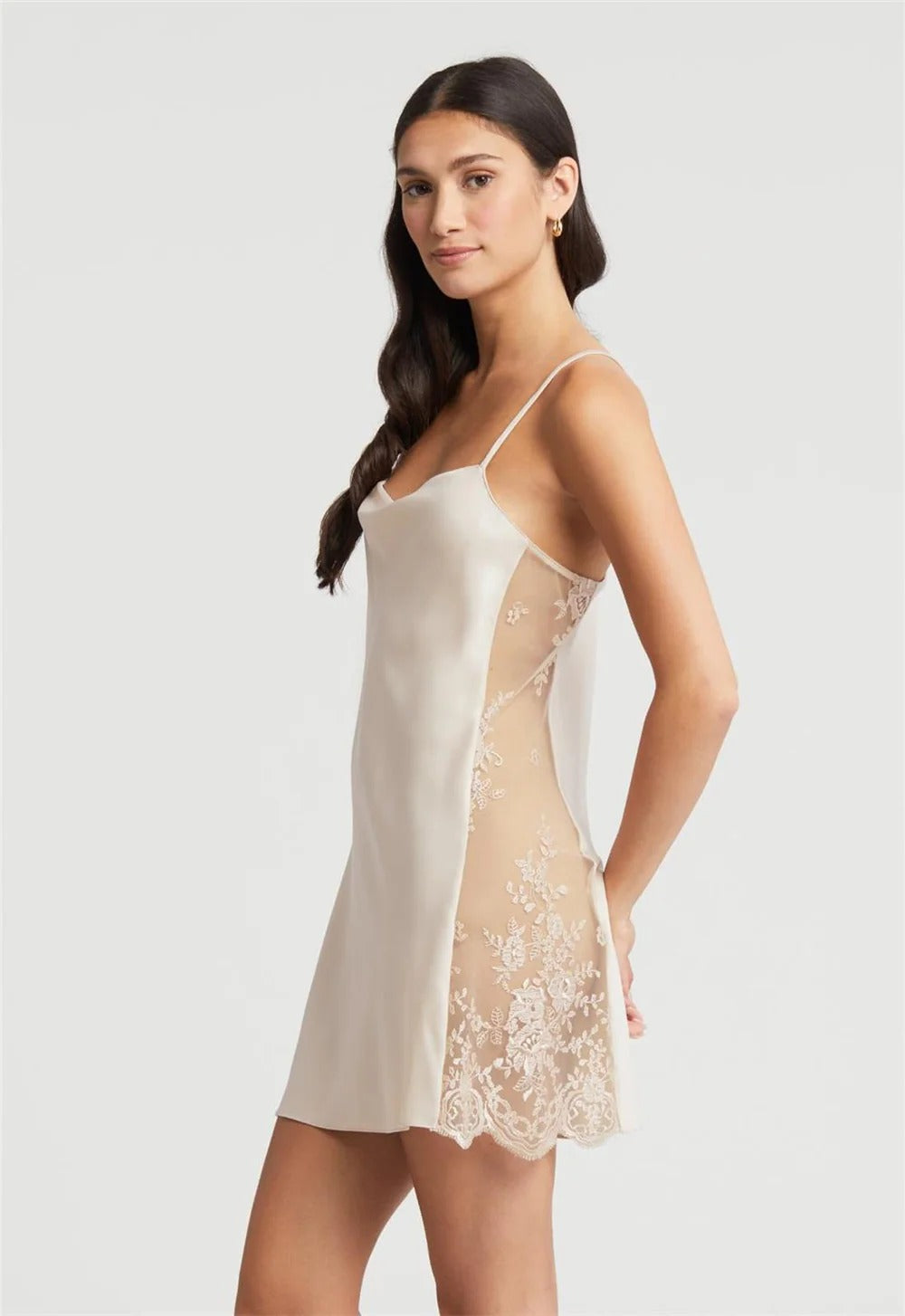 Woman wearing a white slip dress with lace details on a light gray background