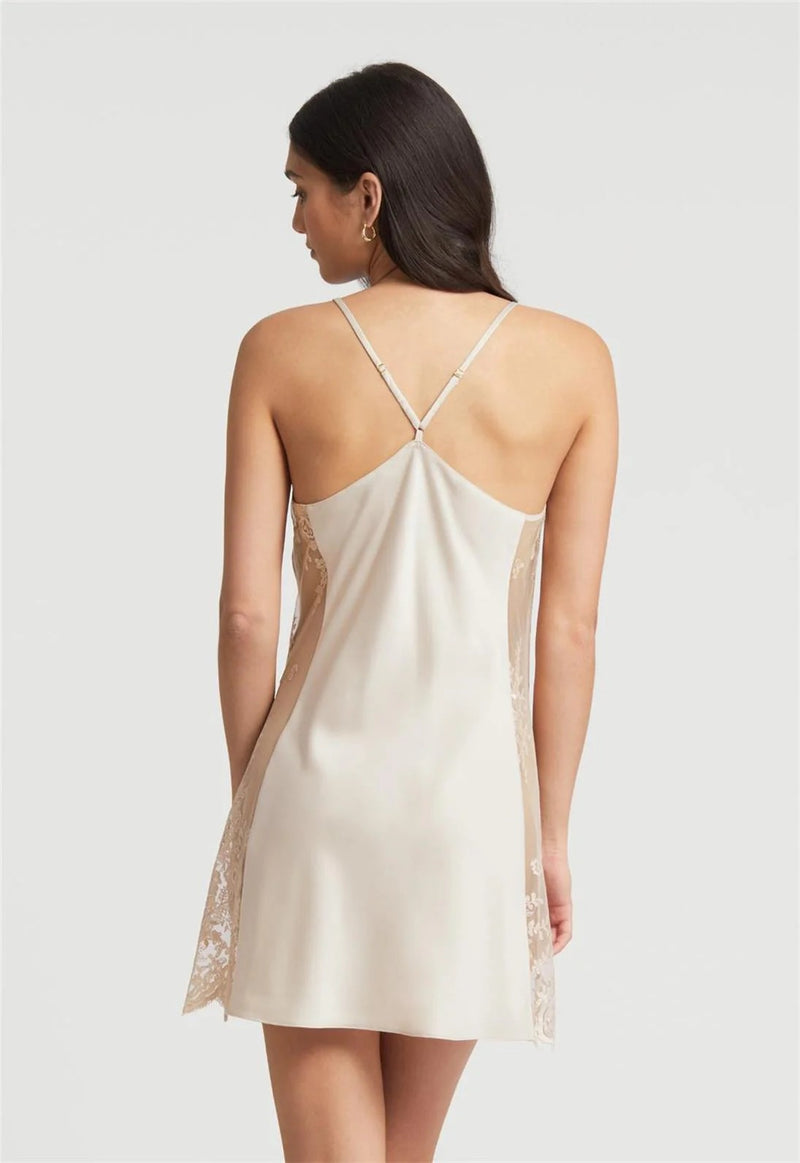 Woman wearing a white slip dress with lace details on a plain background