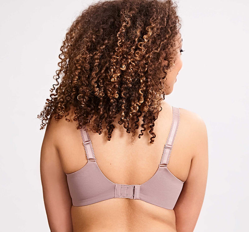 Woman wearing a light purple bralette on a plain background