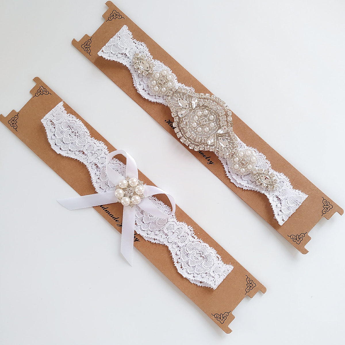 Pair of white lace garters with decorative elements on brown paper packaging.