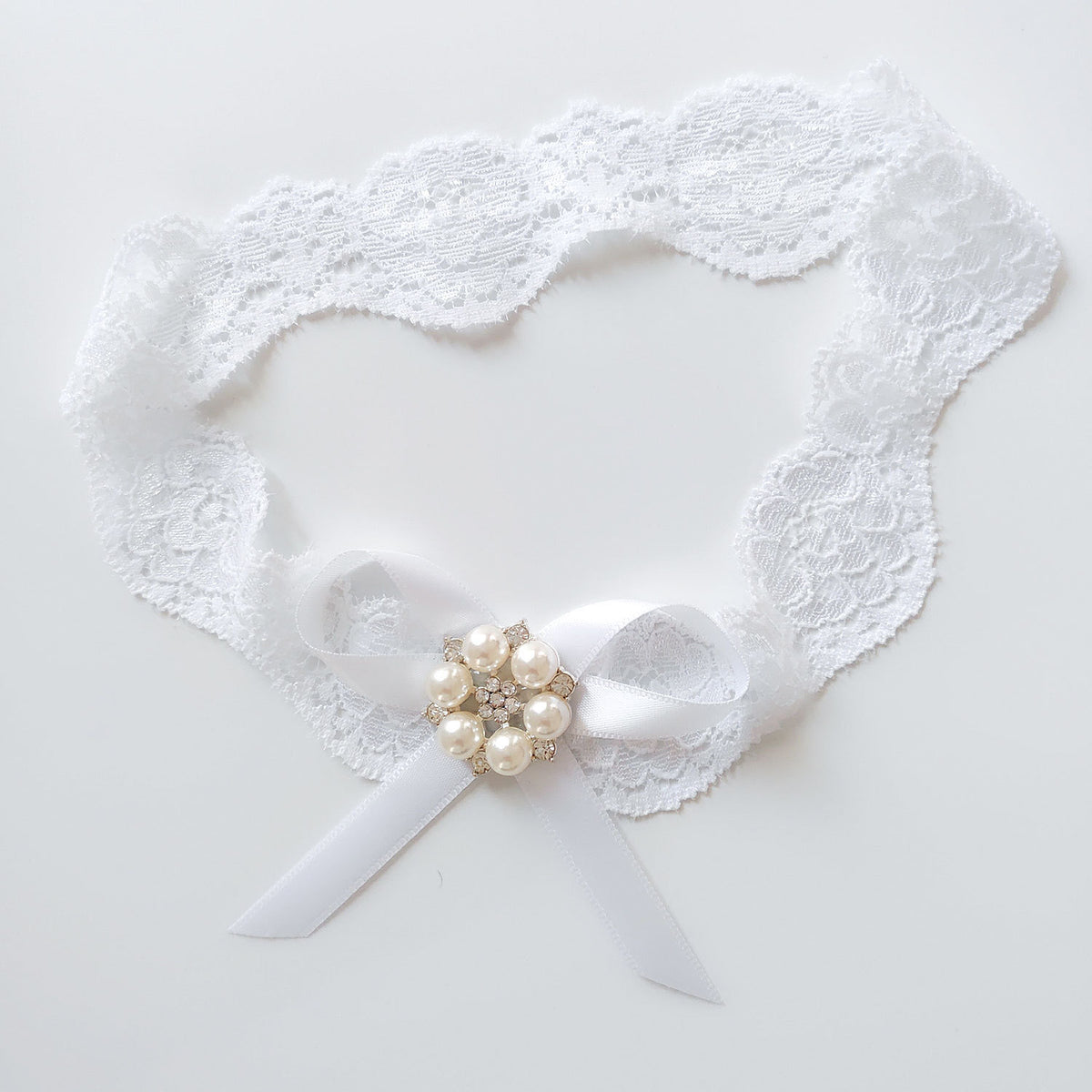 White lace garter with a bow and pearl embellishments on a light gray background