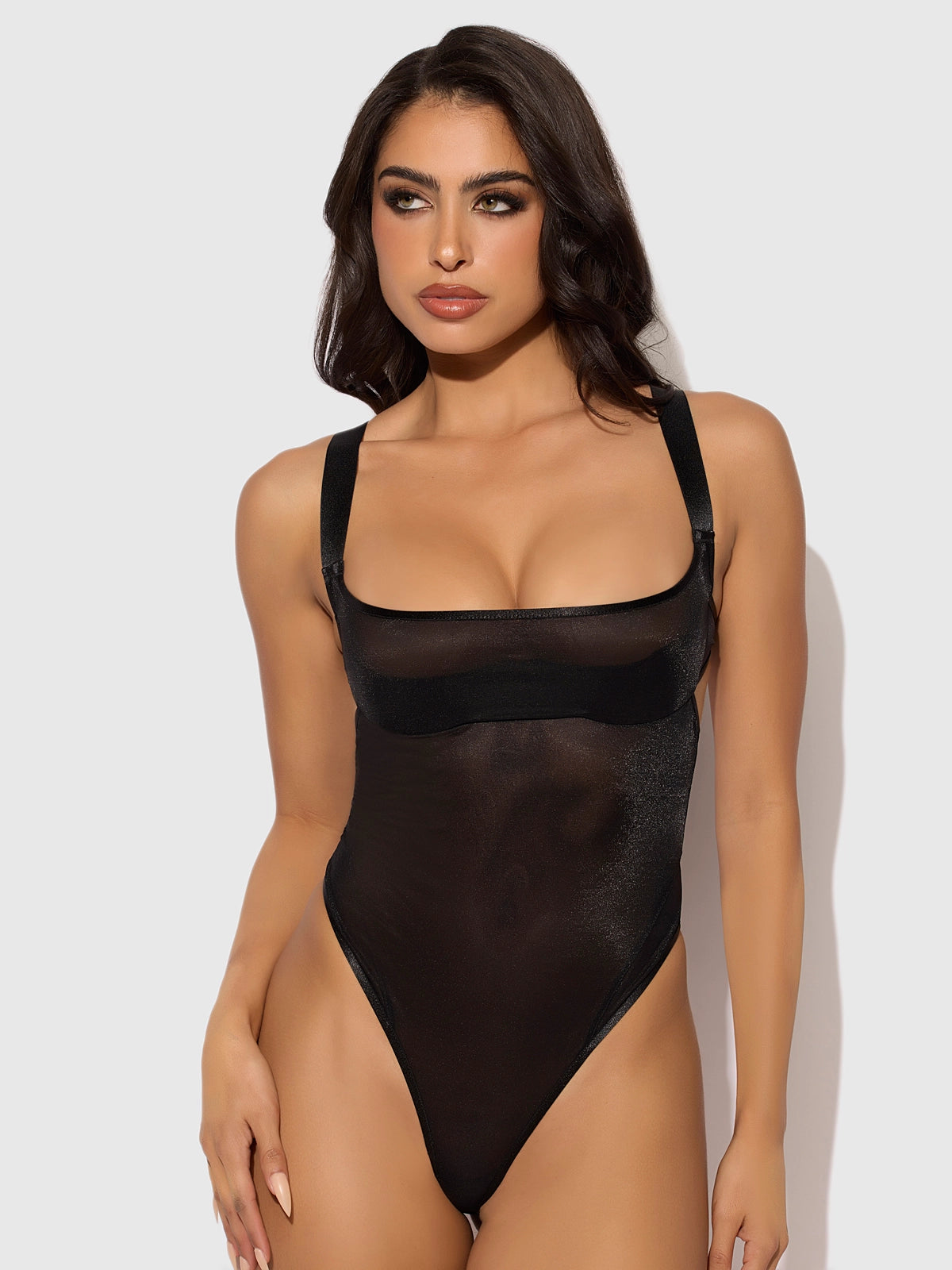 Woman weaing a black Yvone sheer shimmer mesh underwire bodysuit with demi cups, adjustable straps and high-cut tanga bottom.