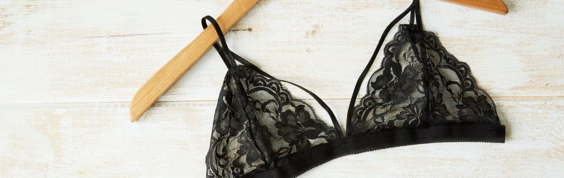 Black lace bra on a wooden hanger against a light wooden background
