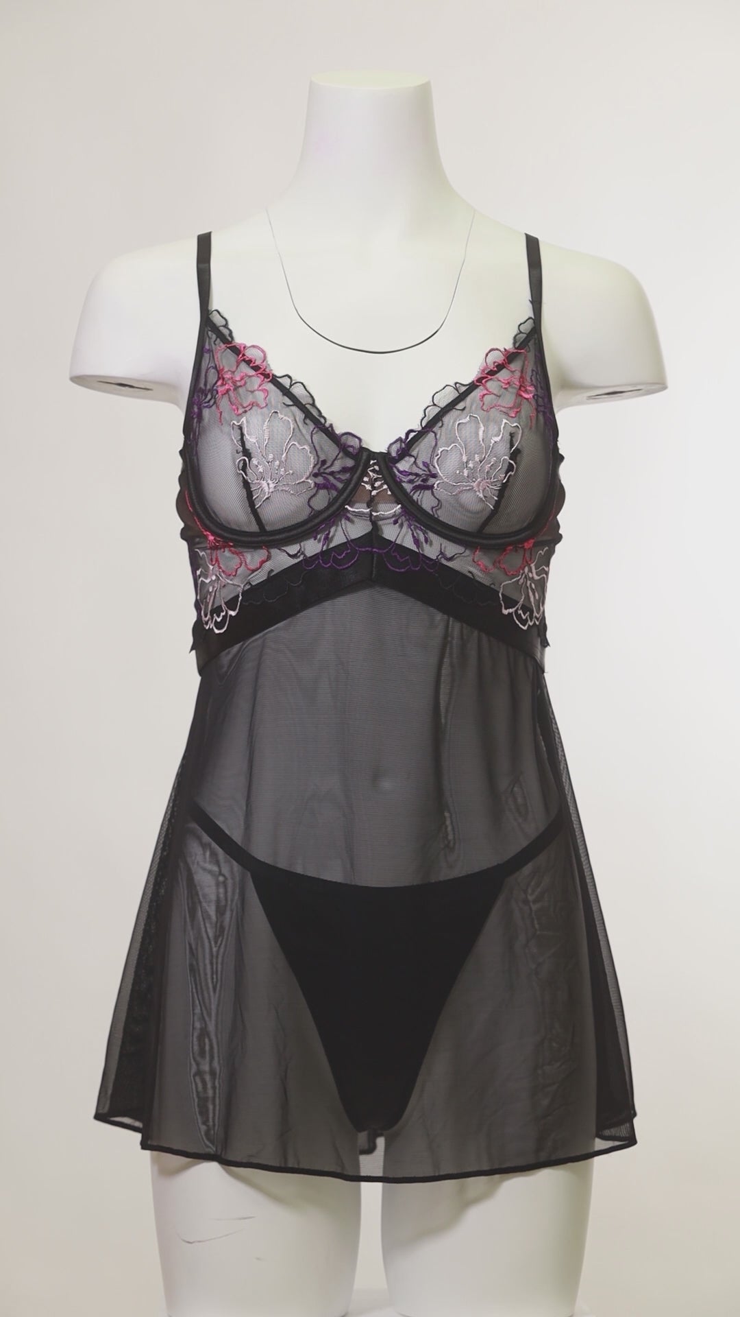 A sheer black lingerie set with floral embroidery on mannequin on a white background